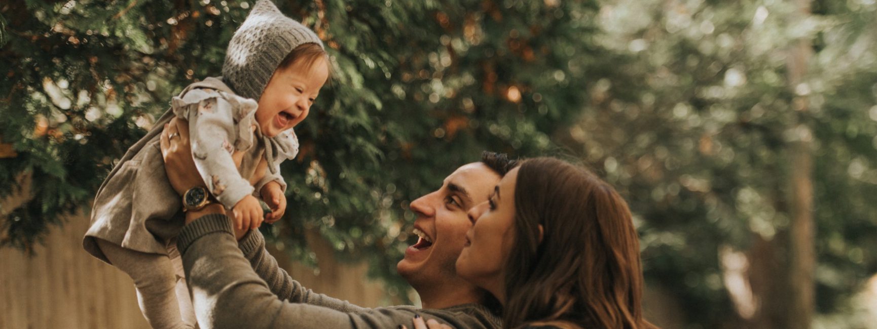 Parents lifting their laughing baby into the air outdoors