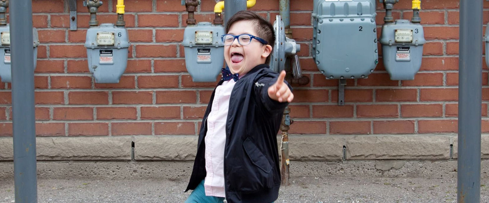 A boy in a bow tie laughing and pointing at the camera